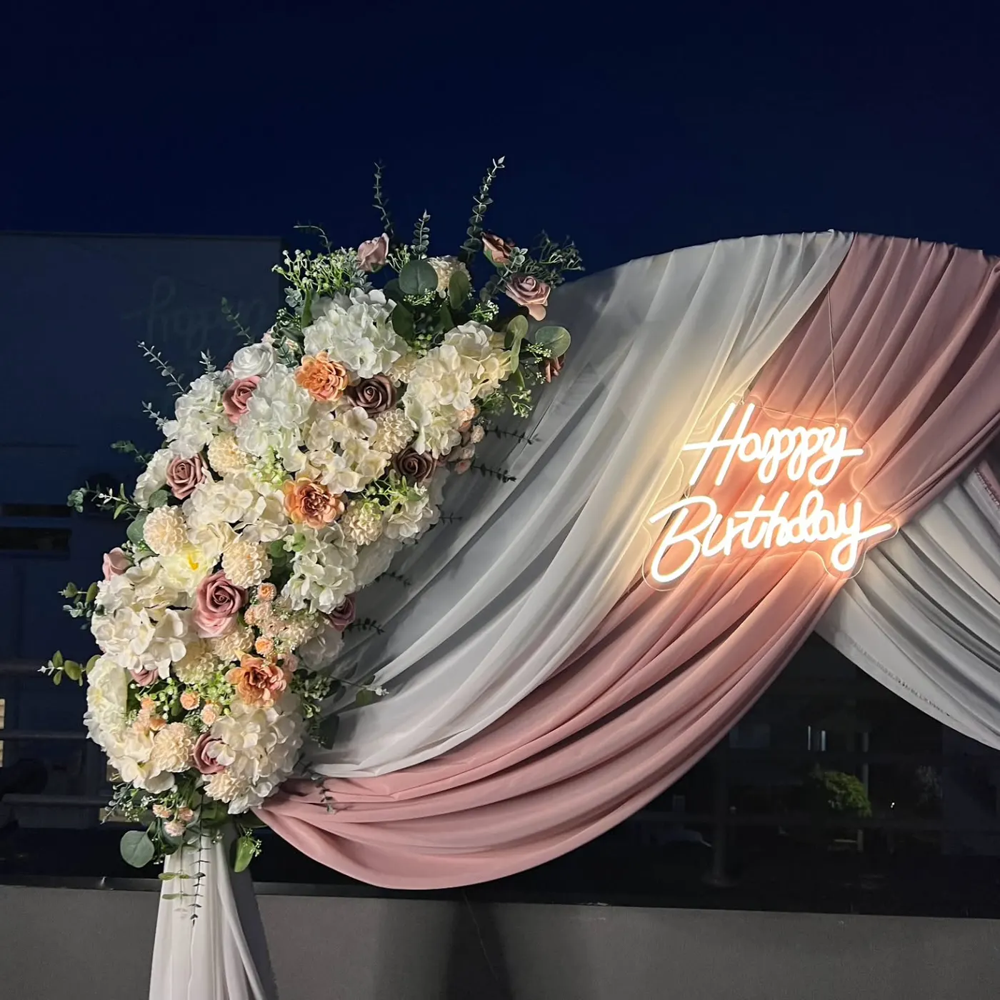 Neonski natpis Happy Birthday na luku sa cvećem u večernjim tonovima