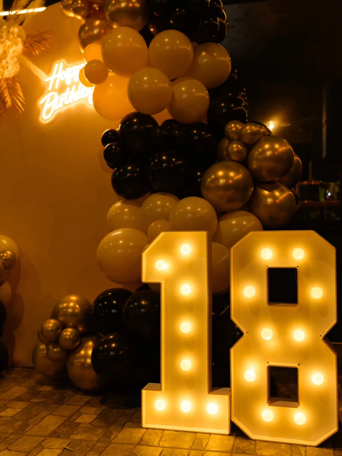 Svetleći broj 18 uz crno-zlatnu balon girlandu — dekoracija punoletstva noću