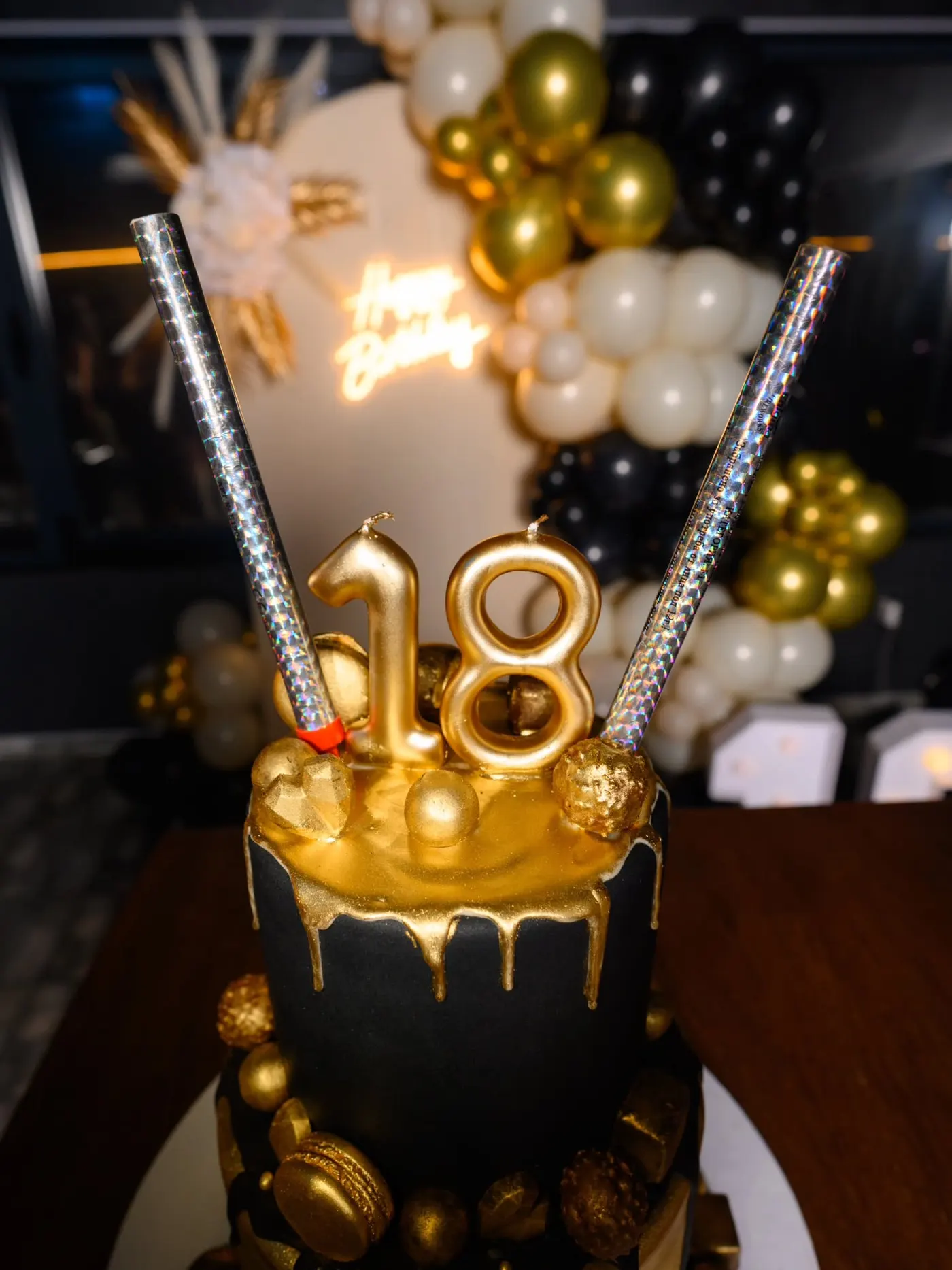 Crno-zlatna torta sa prskalicama ispred balon dekoracije za 18. rođendan