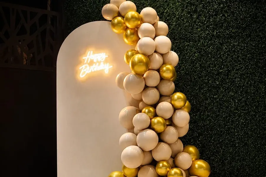 Zlatna kolona balona uz ivory pano sa neonskim natpisom Happy Birthday pored bazena, noću