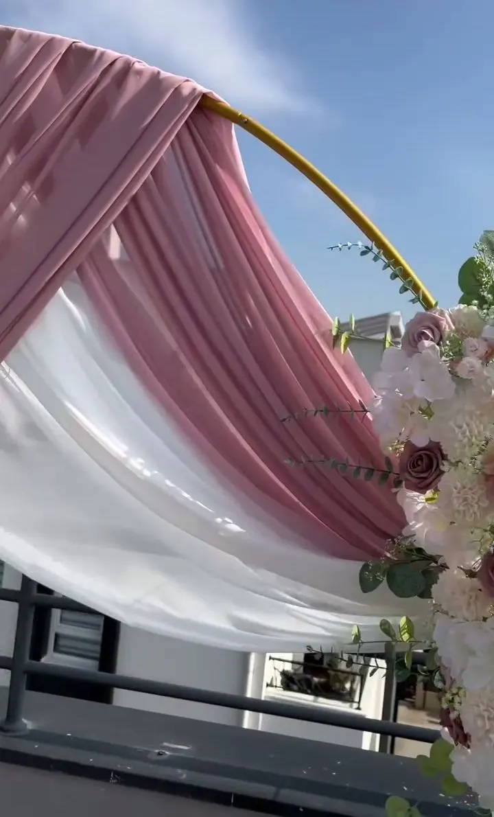Bela i puder roze draperija prebačena preko zlatnog obruča, pod plavim nebom